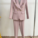Pink suit with gold buttons on a hanger against a plain background