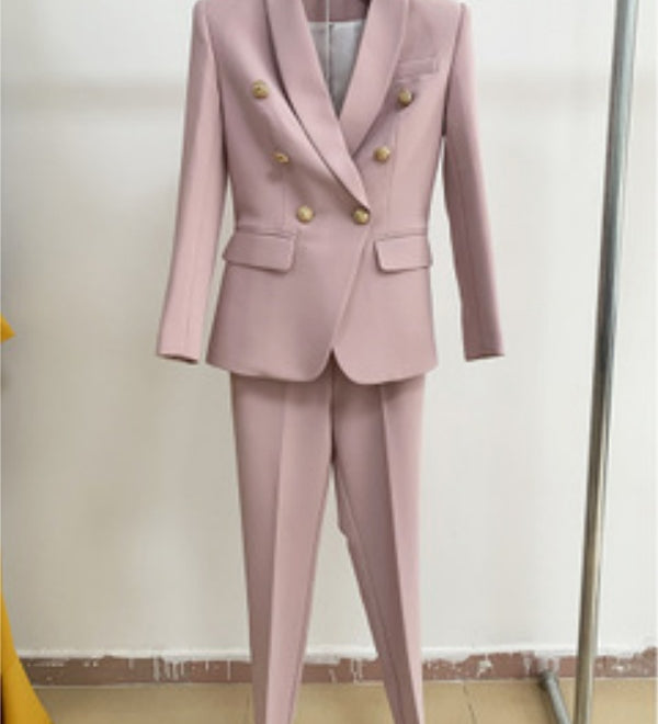 Pink suit with gold buttons on a hanger against a plain background