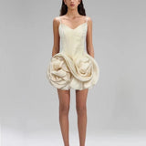 Woman wearing a unique cream-colored dress with a large floral embellishment on a plain background