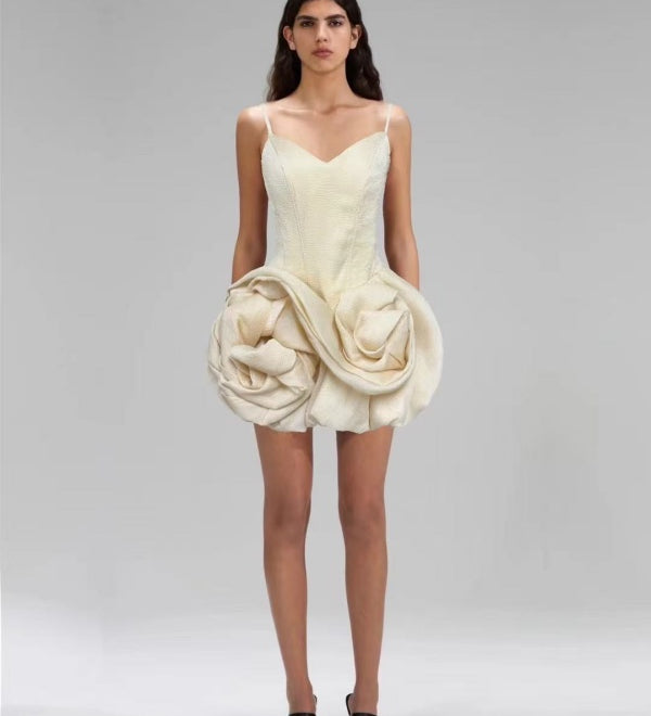 Woman wearing a unique cream-colored dress with a large floral embellishment on a plain background