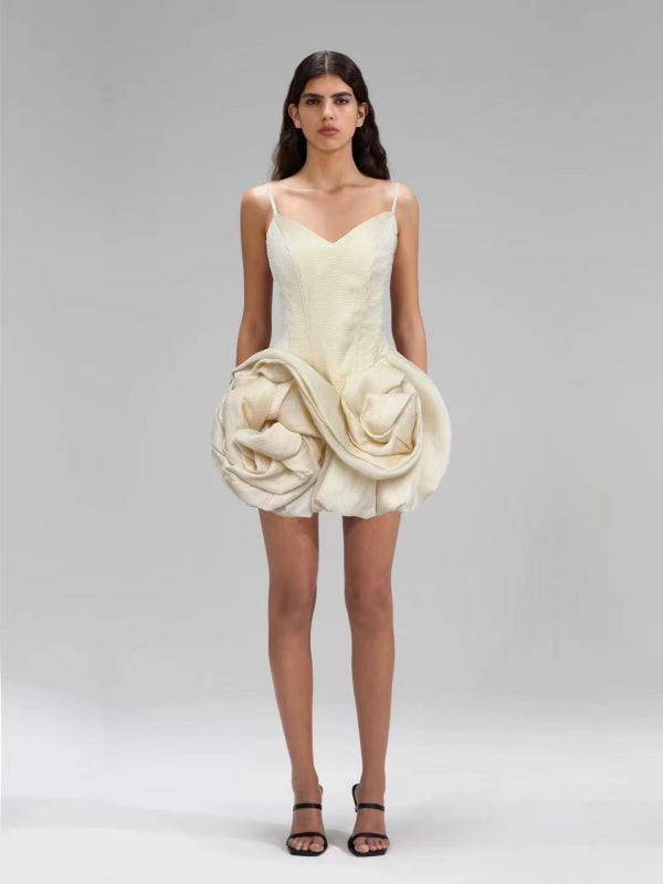 Woman wearing a unique cream-colored dress with a large floral embellishment on a plain background