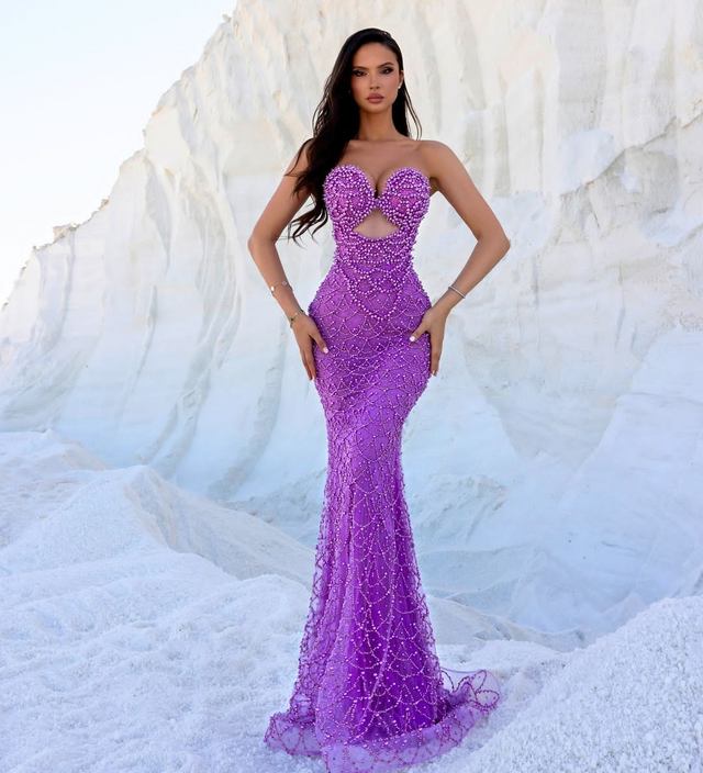 Woman wearing a glamorous amethyst beaded mermaid gown with sweetheart neckline and intricate detailing, posing against a white rocky background
