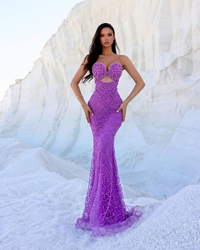 Woman wearing a glamorous amethyst beaded mermaid gown with sweetheart neckline and intricate detailing, posing against a white rocky background
