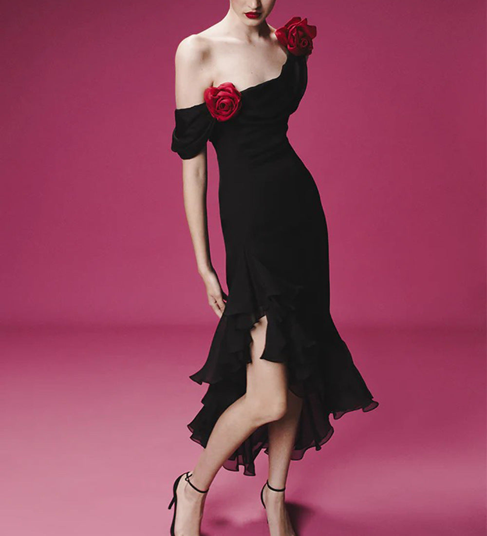 Woman in a romantic off-shoulder black dress with red rose accents and layered ruffles, standing against a pink background