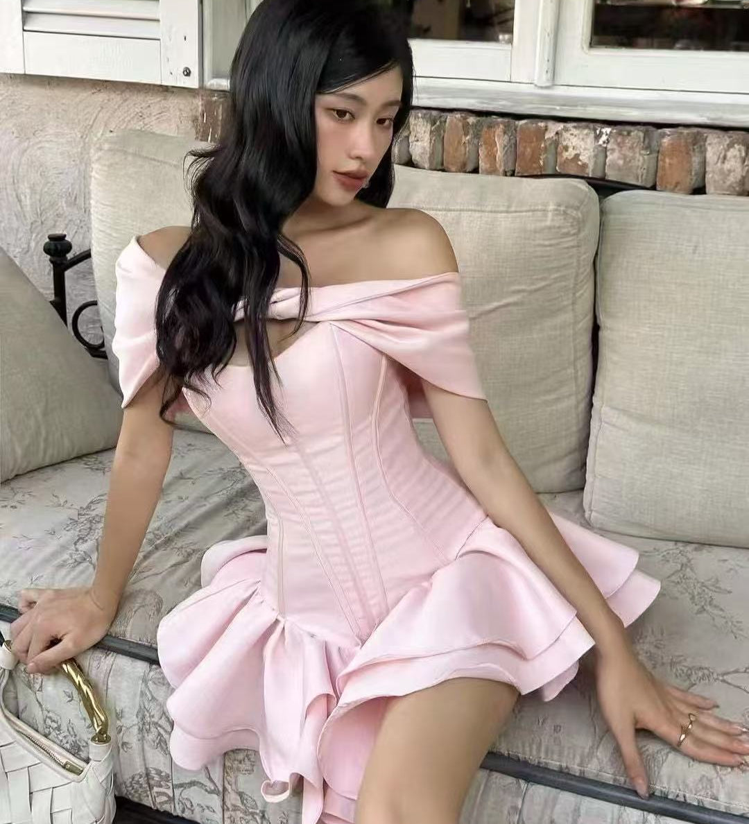 Blush pink off-shoulder corset mini dress with double ruffle hem worn by model sitting on a couch—EtiquetteMode romantic party wear