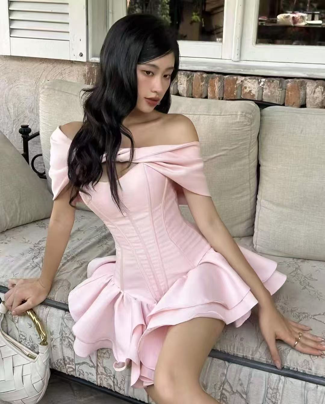 Blush pink off-shoulder corset mini dress with double ruffle hem worn by model sitting on a couch—EtiquetteMode romantic party wear