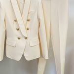 White suit jacket with gold buttons and matching pants on a hanger against a white background