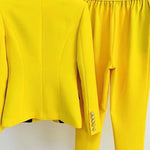 Yellow suit jacket and pants on hangers against a white background