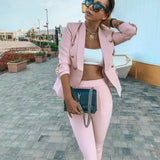 Woman in pink outfit with sunglasses and handbag on a paved walkway.