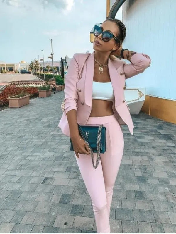 Woman in pink outfit with sunglasses and handbag on a paved walkway.